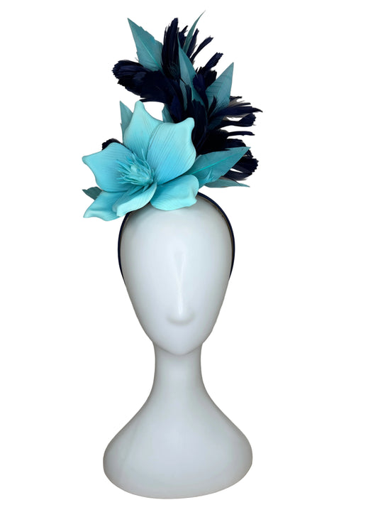 White vase with blue flowers and black feathers on a beige background