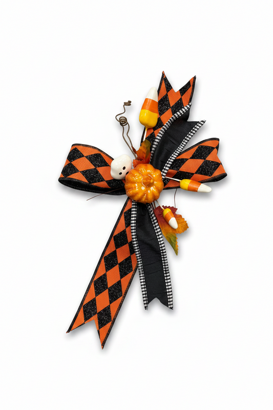 A Halloween-themed decorative bow made from black and orange checkered ribbon, with candy corn pieces, a small orange pumpkin, a white skull ornament, and a black-and-white striped ribbon accent.